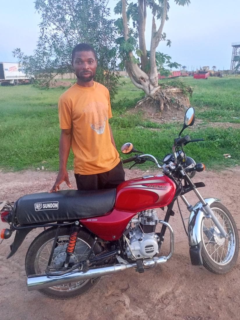A programme beneficiary standing beside the motorcycle he received